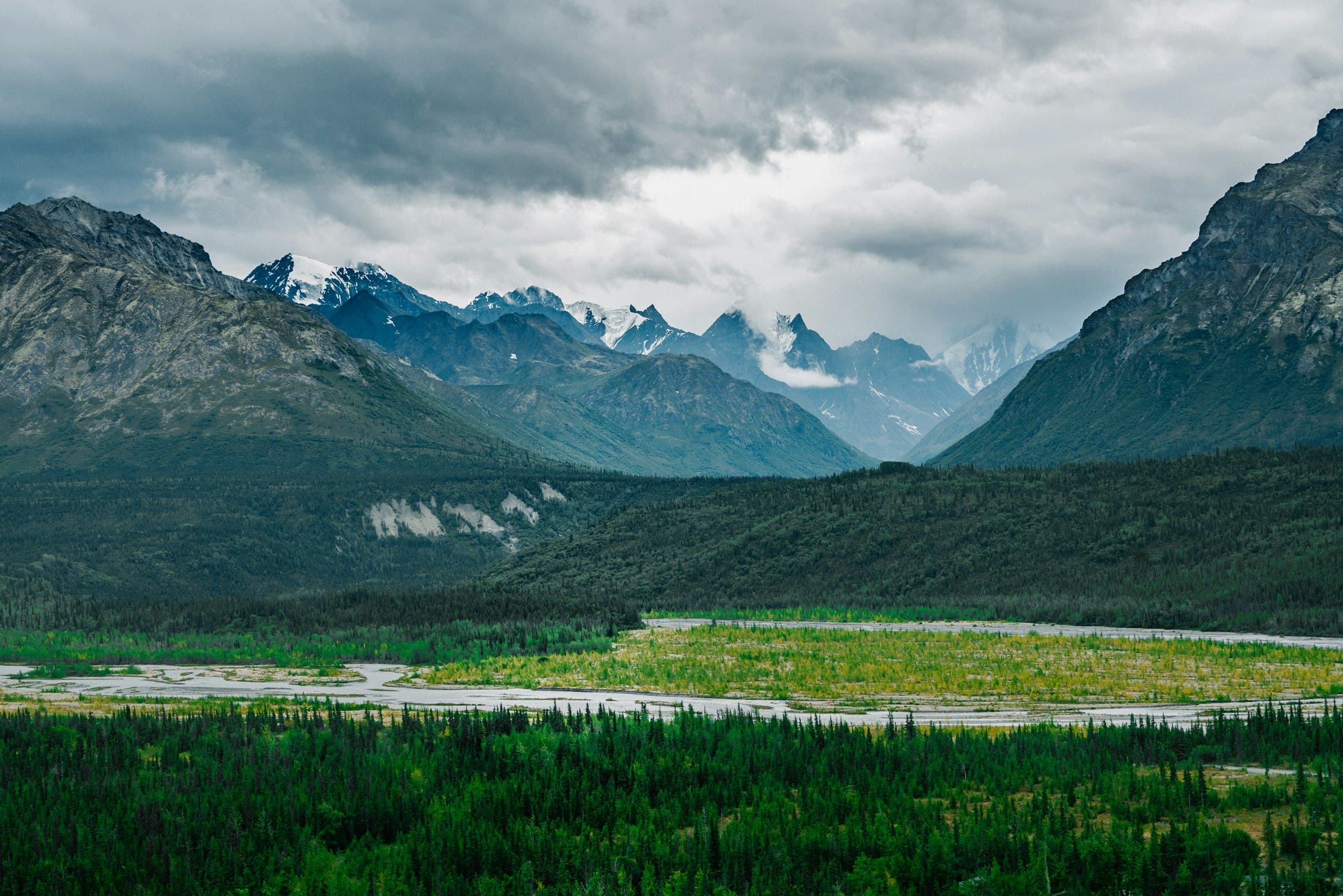 Green valley and mountain range under a cloudy Alaska sky